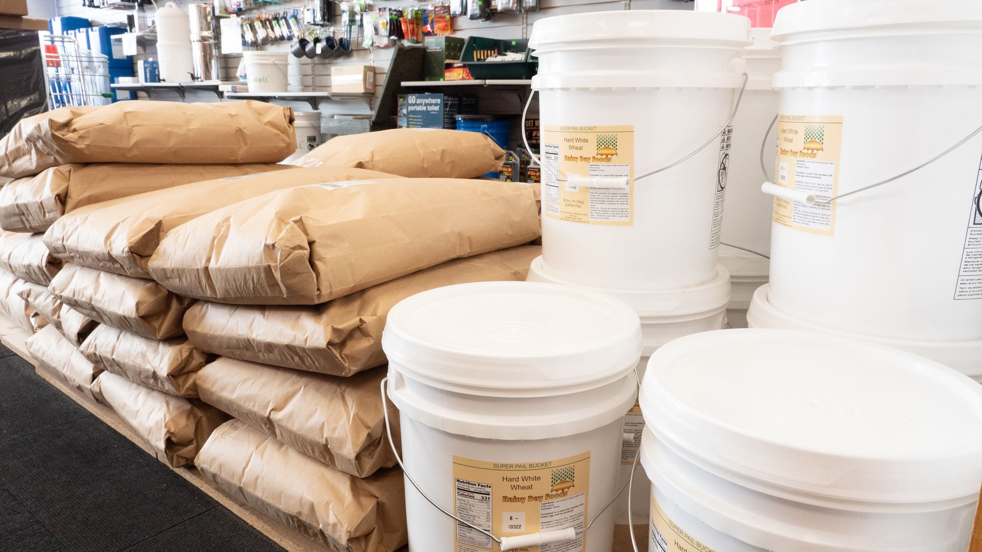 Bags of brown paper and white buckets on display inside a store, possibly containing ingredients or supplies.