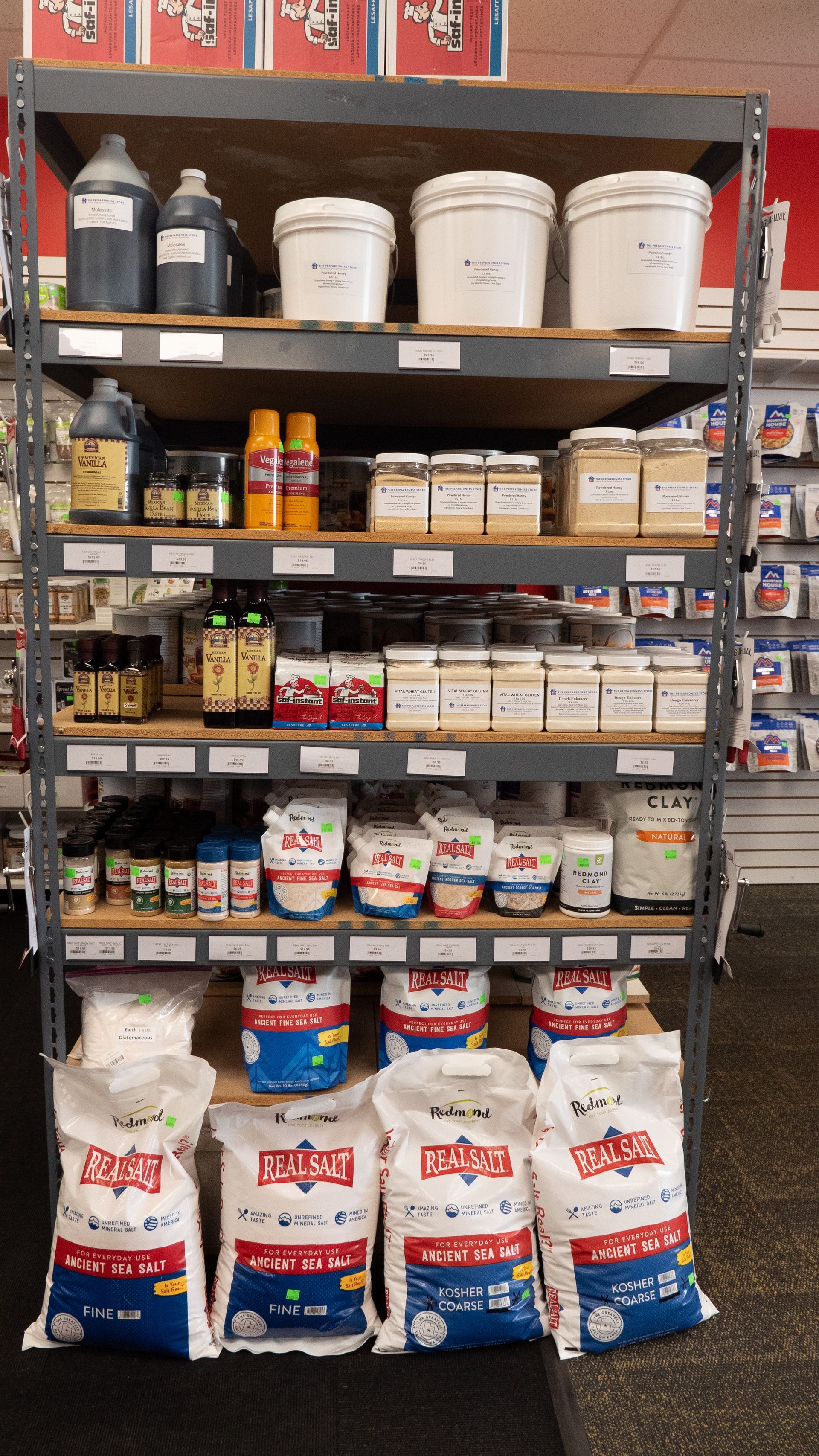 A metal shelving unit filled with various containers, buckets, and bags of products, likely for sale in a store.