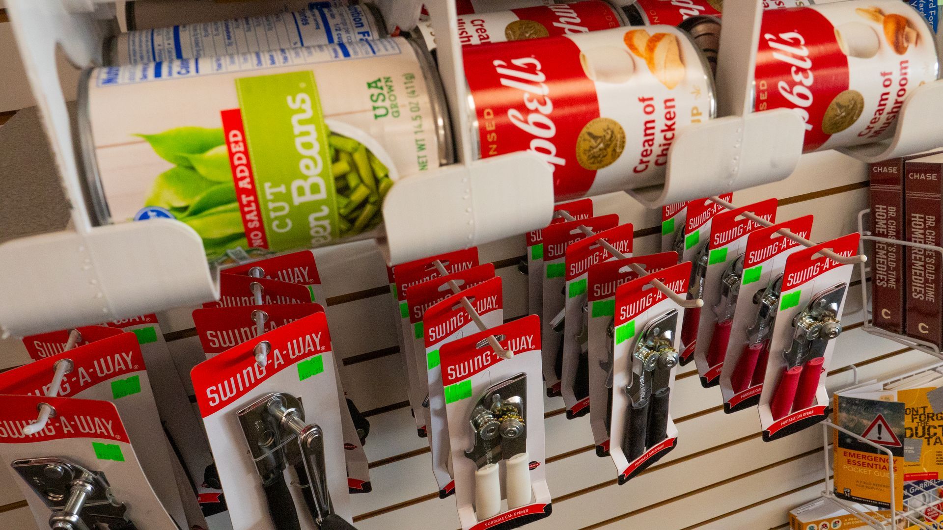 Canned goods and can openers for sale in a store. Campbell's soup cans sit above hanging can openers.