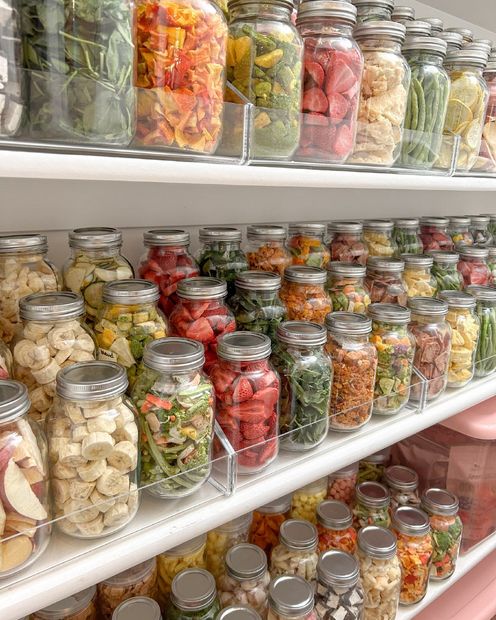 Shelves lined with numerous glass jars containing preserved, colorful fruits and vegetables.