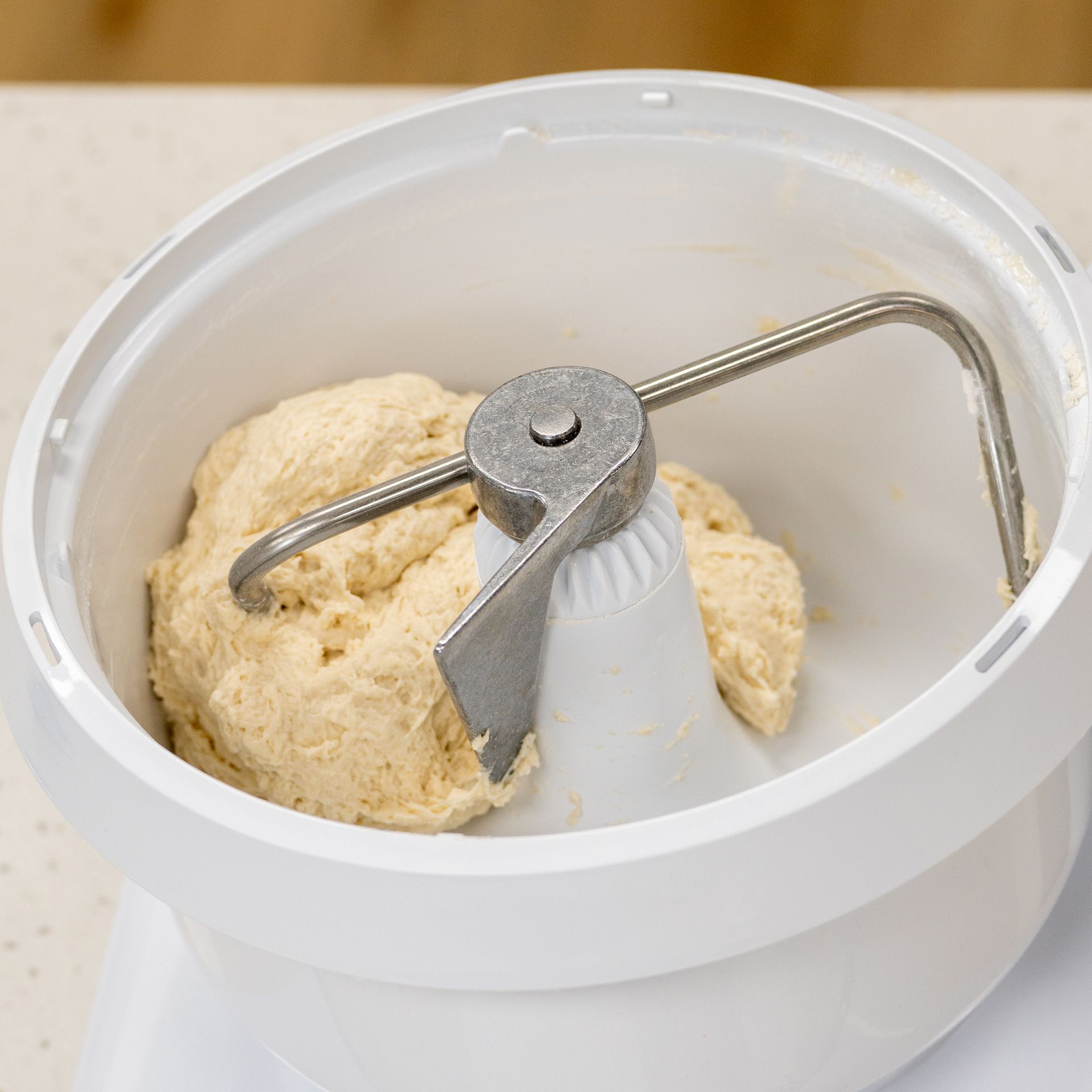 Dough in a white kitchen mixer being mixed with a metal dough hook.