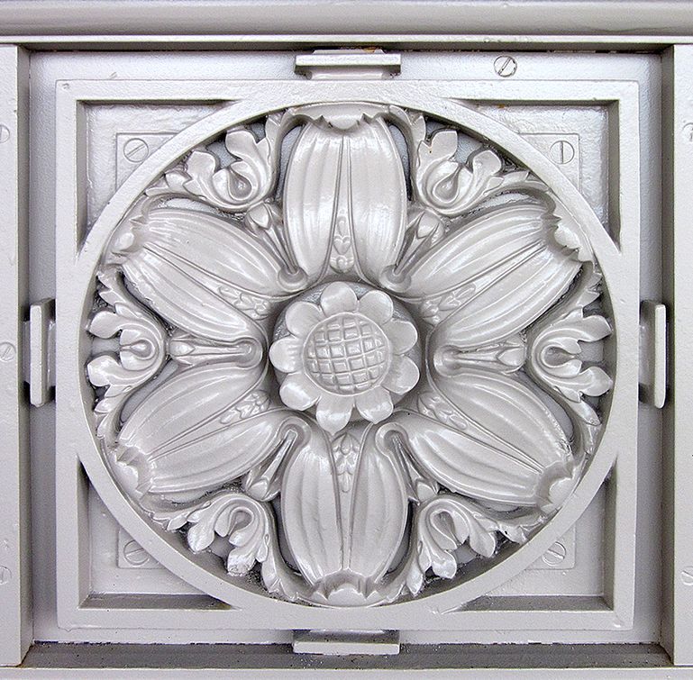 A monochromatic, circular floral architectural carving with a detailed center, set within a square frame.