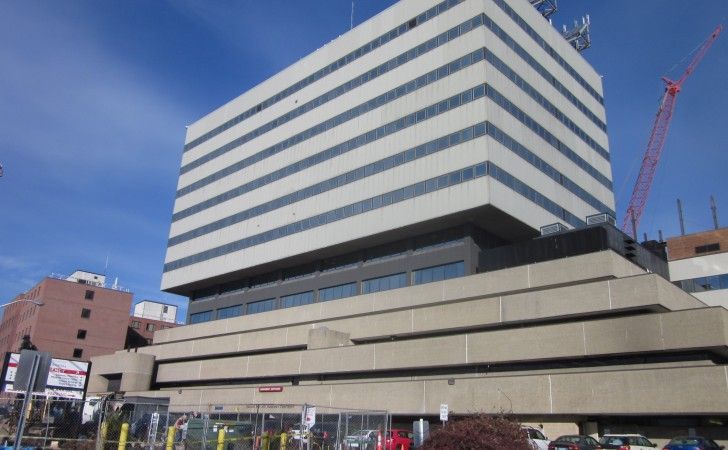 A multi-story commercial building with a terraced concrete base and a tall, glass-paneled tower under a clear blue sky.