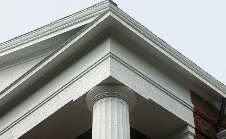A close-up view of the white exterior corner of a building featuring a fluted column, decorative molding, and a pediment.