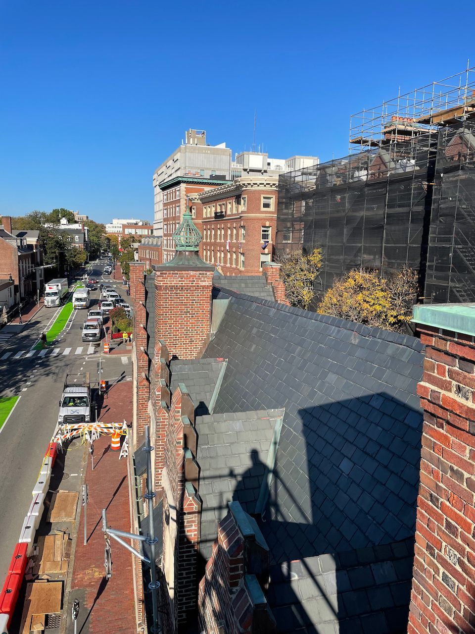 A high-angle view looking down at a slate roof, brick architecture, and a construction site along a city street.