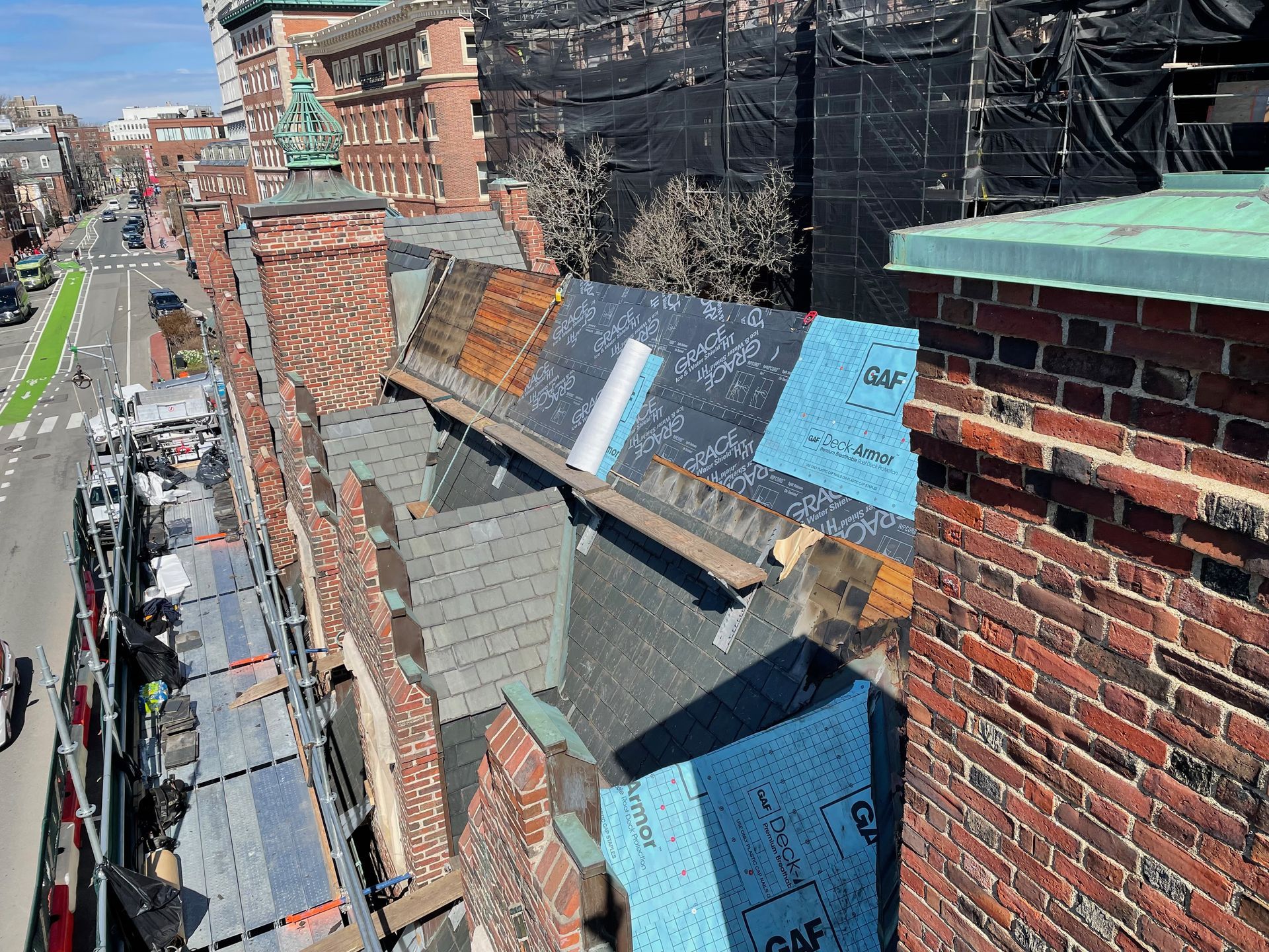 A high-angle view of a building roof undergoing construction, featuring blue and grey underlayment and brick chimneys.