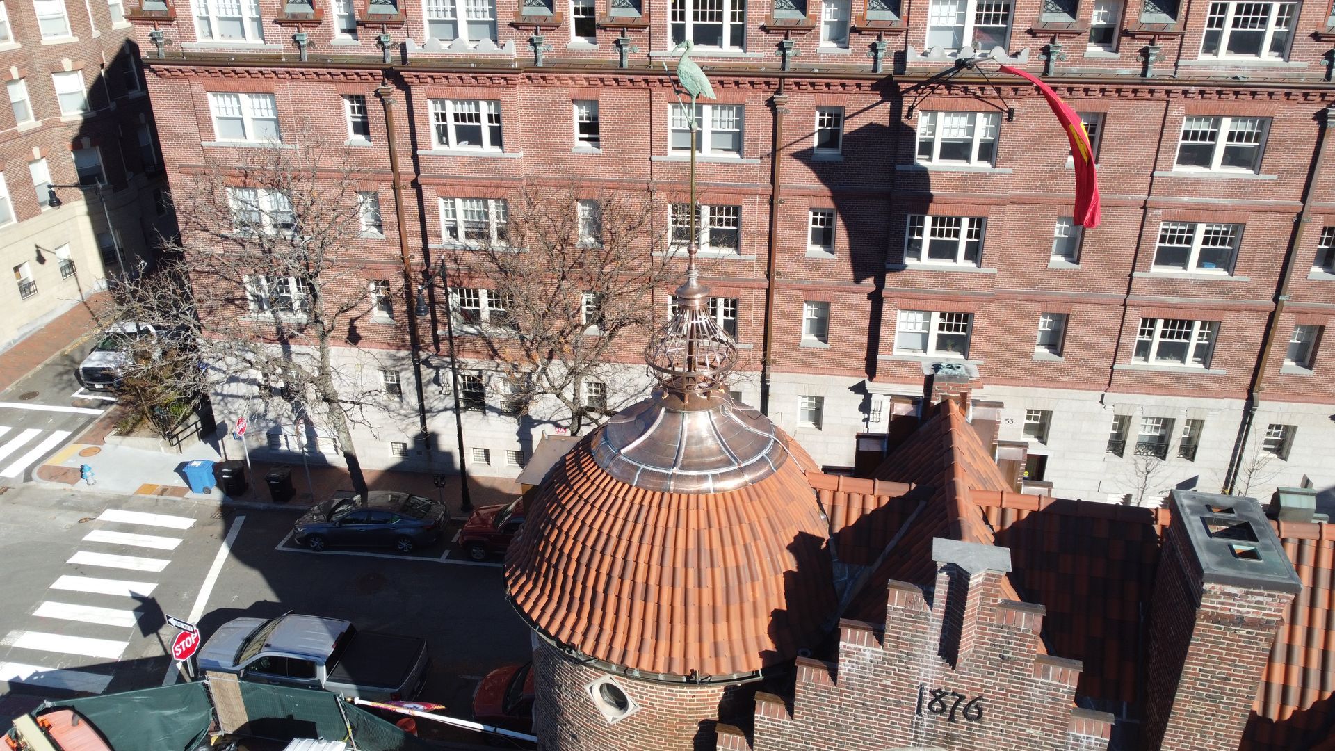 High-angle view of a red brick building with a copper-roofed turret and a stepped gable marked 
