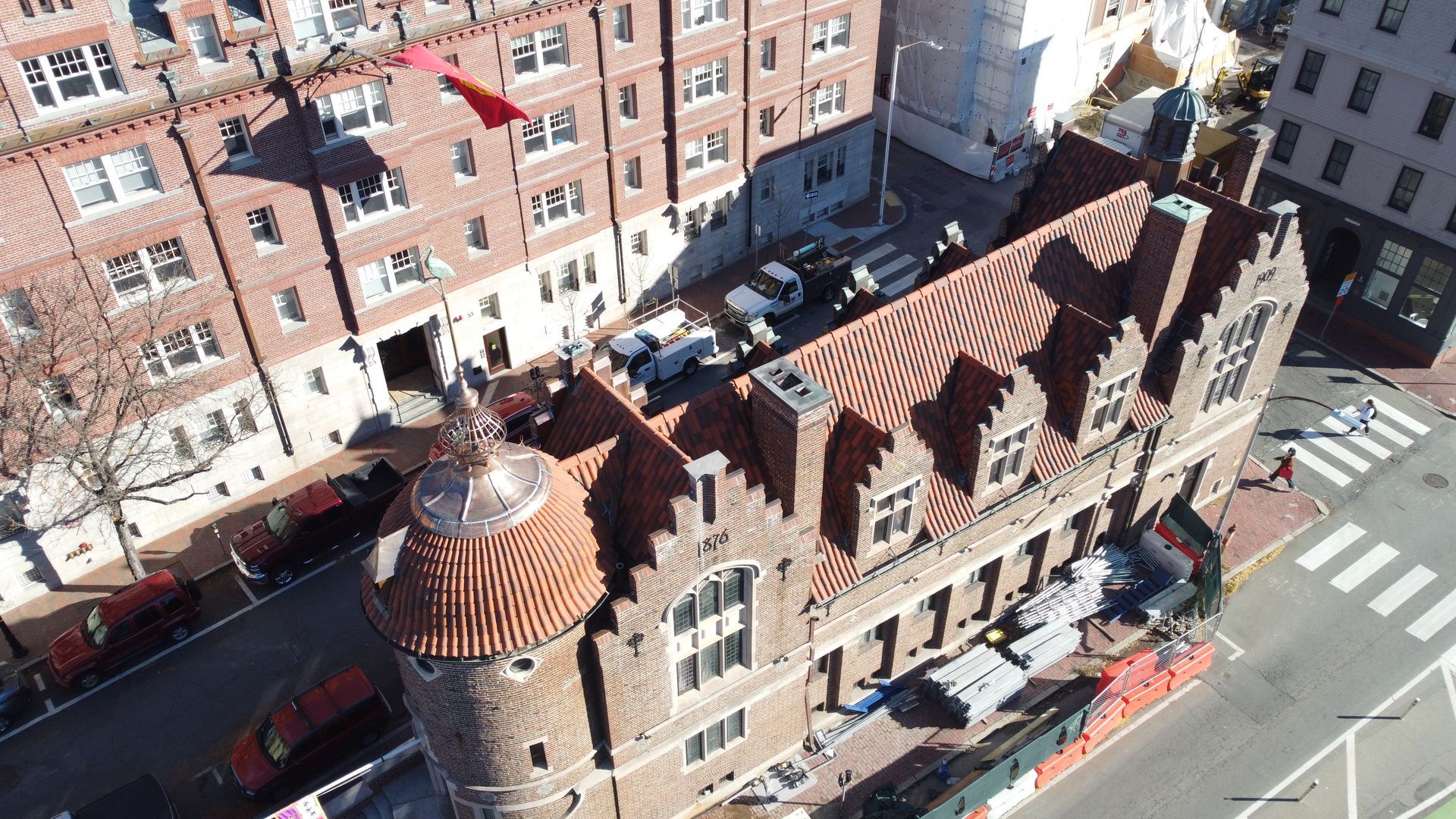 Aerial view of a brick building with a rounded tower and tiled roof during construction, surrounded by city streets.