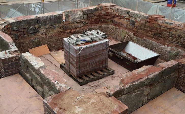 A construction site featuring weathered brick walls, a wooden pallet holding stacked bricks, and a metal mortar box.