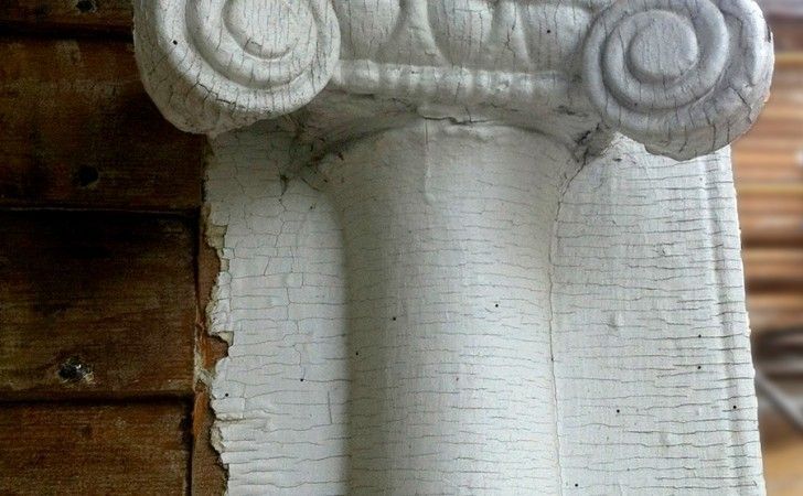 Close-up of a white painted architectural column capital with cracked, peeling paint next to wooden siding.