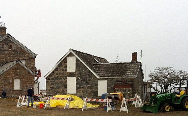 Construction work on two historic stone buildings with yellow tarps and a green tractor on a cloudy day.