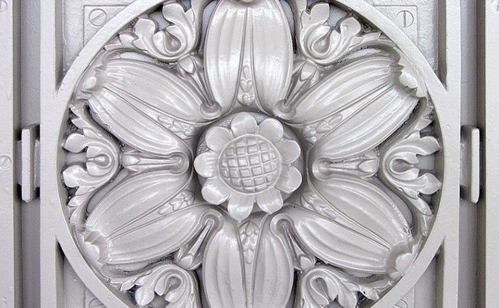 A close-up of a circular, cream-colored architectural relief featuring a central daisy-like flower surrounded by petals.