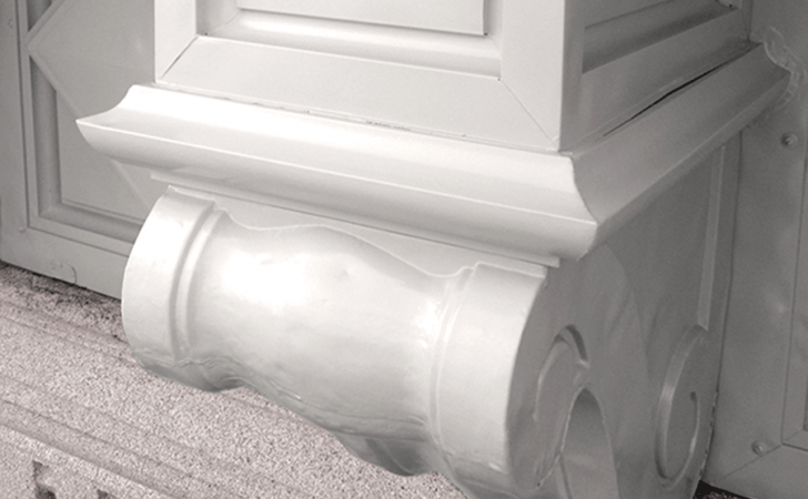 A close-up view of an ornate, white architectural corbel or bracket mounted on a textured wall.