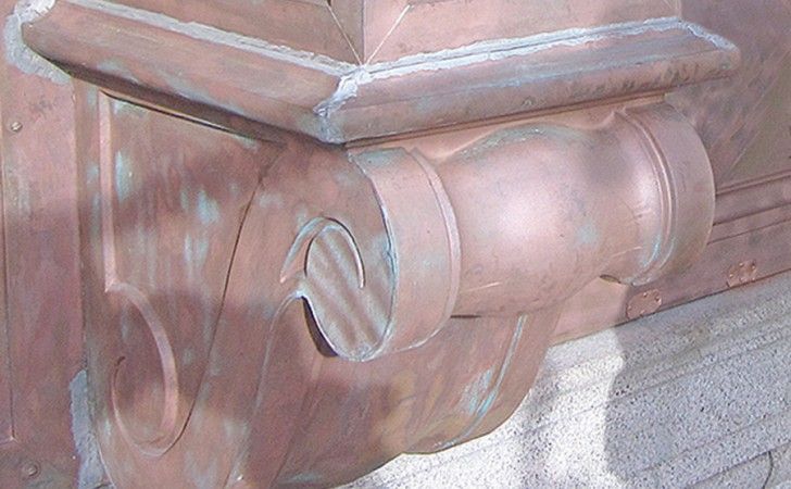 A decorative copper bracket with scroll details and signs of verdigris patina supporting a horizontal ledge.