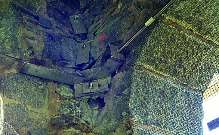 A metal reinforcement bracket anchored into a stone wall corner to stabilize masonry.