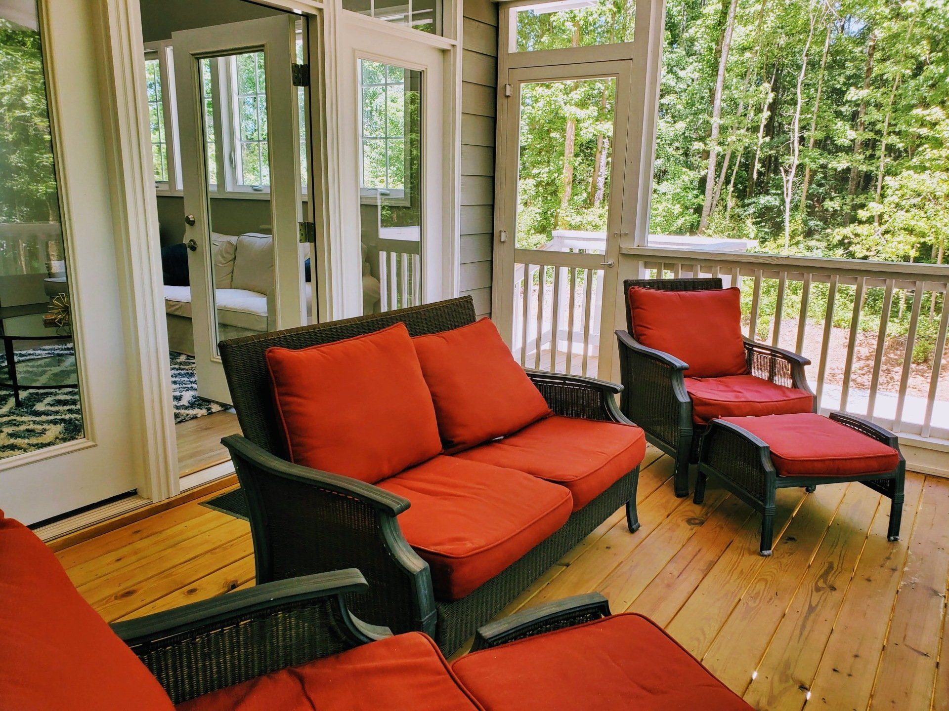 A porch with a couch and chairs with red cushions