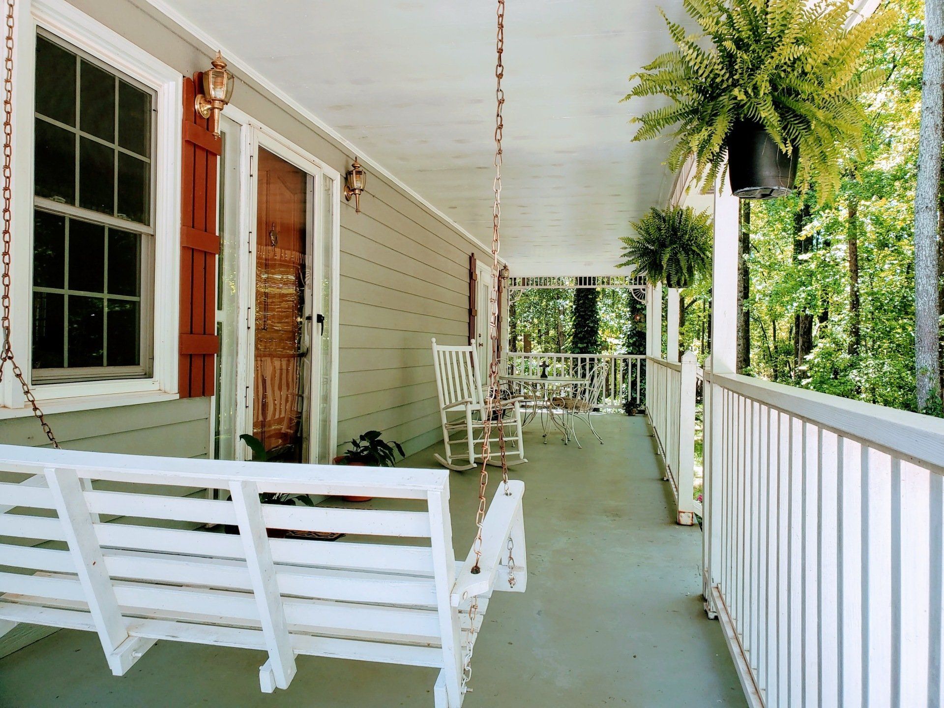 A porch with a white swing and rocking chairs