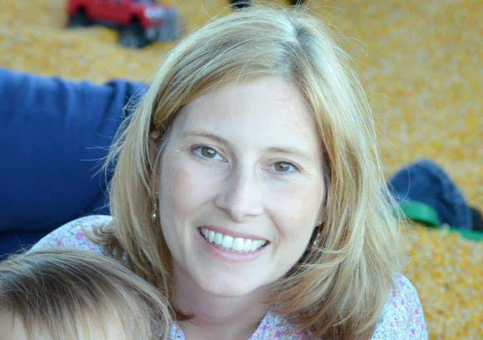 A woman is smiling while holding a baby in her arms.