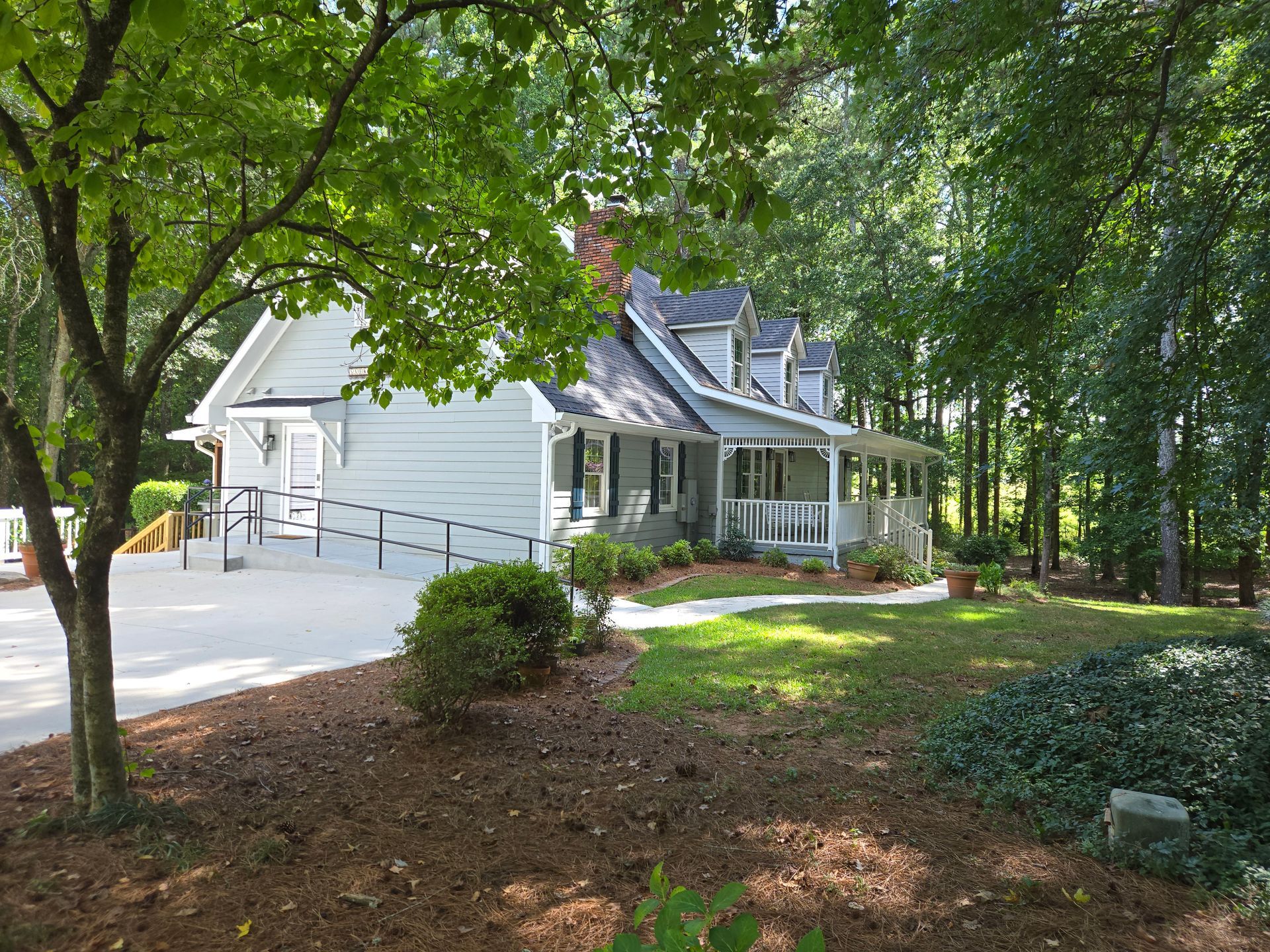 A white house with a handicap ramp is surrounded by trees.