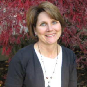 A woman wearing a black cardigan and a white shirt smiles in front of red leaves