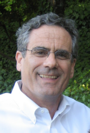 A man wearing glasses and a white shirt smiles for the camera