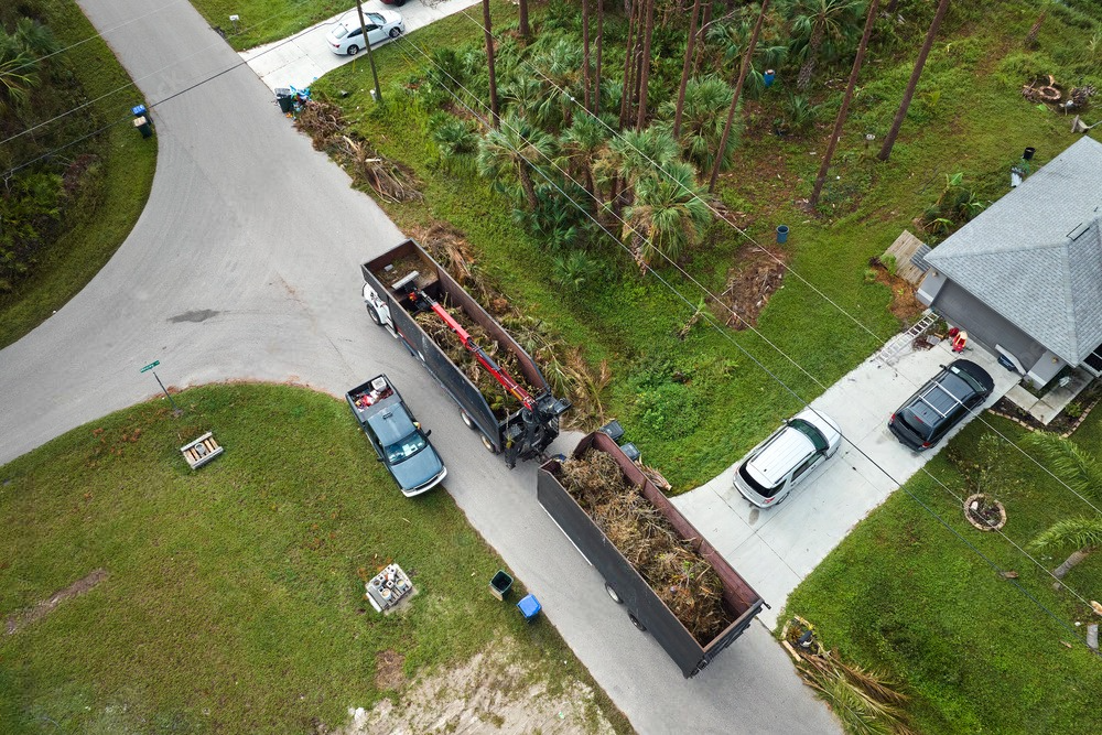 an aerial view of a truck carrying a dumpster down a street next to a house .