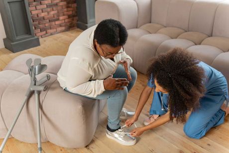 Curly young nurse lacing sneakers of woman with leg injury