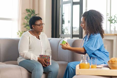 Sick dark-skinned elderly lady looking at nurse giving her some pills