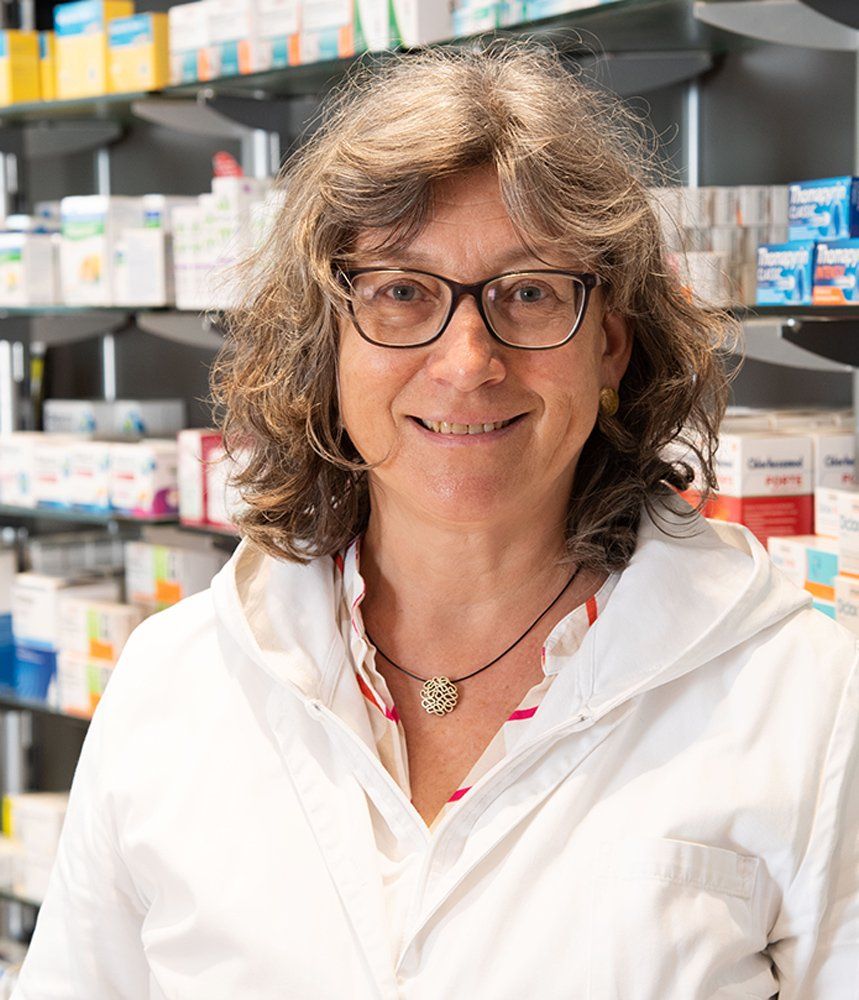 Eine Frau mit Brille und weißem Kittel steht in einer Apotheke.