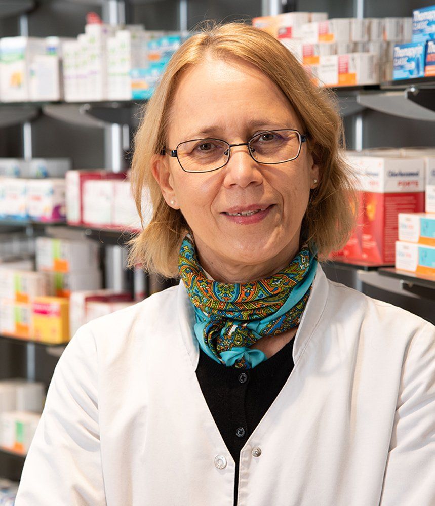 Eine Frau mit Brille und Kopftuch steht in einer Apotheke.