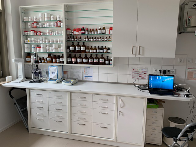 Ein Labor mit vielen Flaschen auf Regalen und einem Laptop auf einem Schreibtisch.