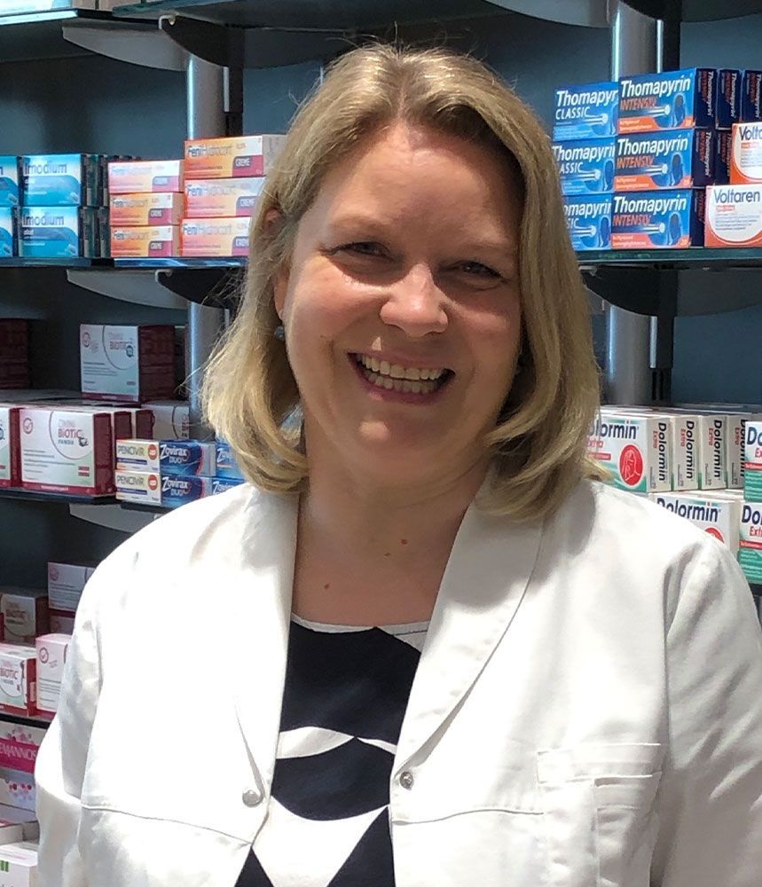 Eine Frau im weißen Kittel lächelt in einer Apotheke.