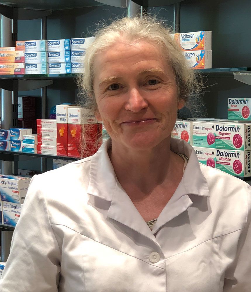 Eine Frau im weißen Kittel steht vor einem Regal mit Pillen.