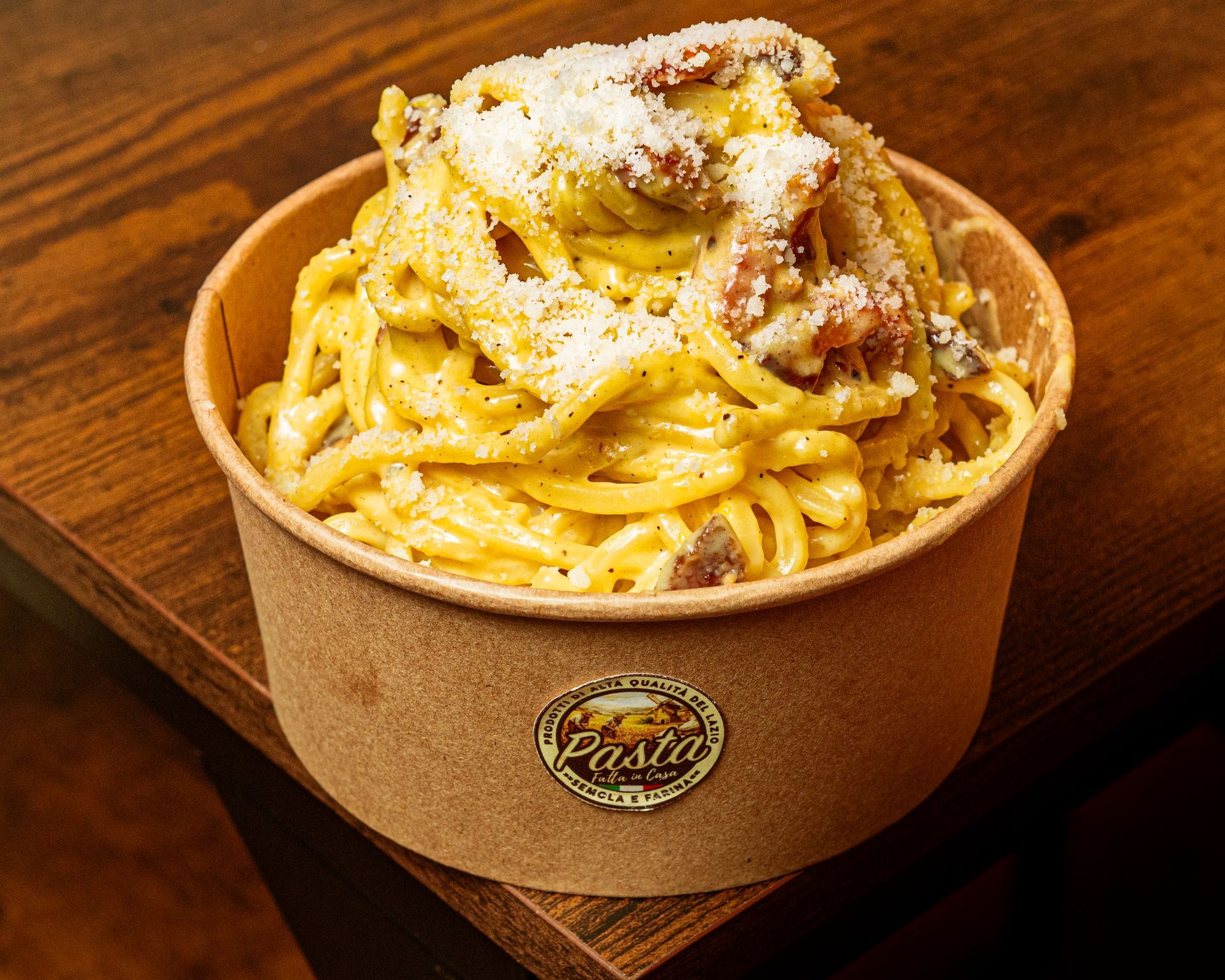 Pasta cremosa condita con formaggio grattugiato, pepe nero e pezzetti di pomodoro su un piatto bianco.