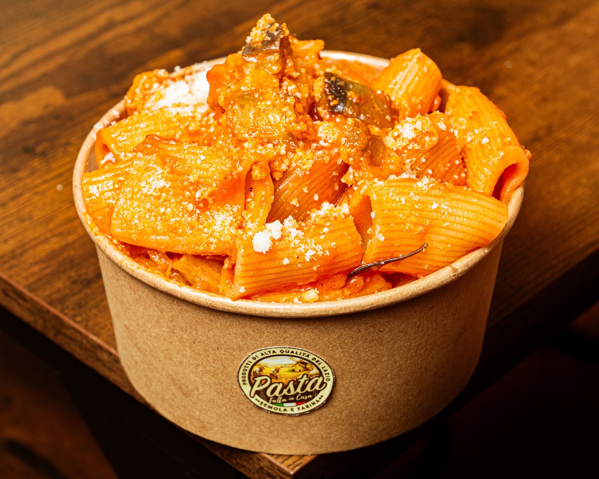 Una ciotola di rigatoni al sugo di pomodoro con polpette su un tavolo di legno.