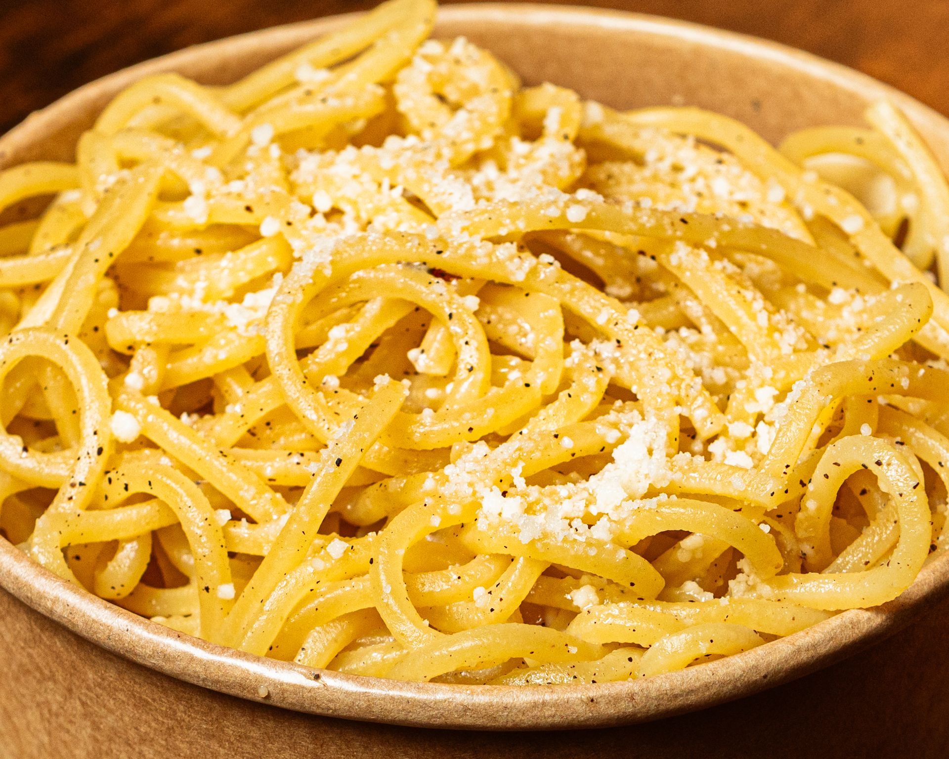 Piatto di spaghetti conditi con formaggio grattugiato su un tavolo di legno.