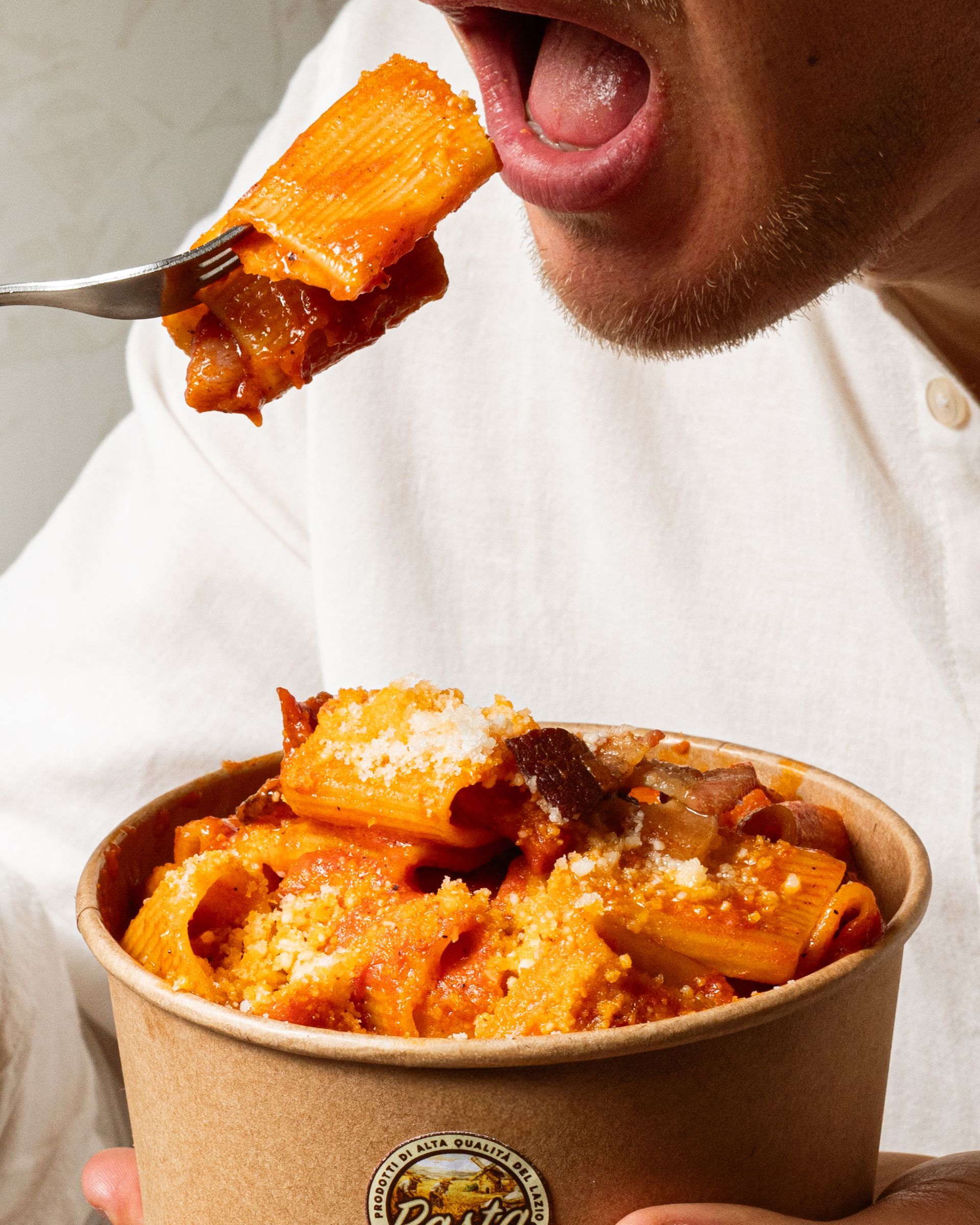 Persona che mangia pasta con salsa all'arancia da una ciotola da asporto con la forchetta