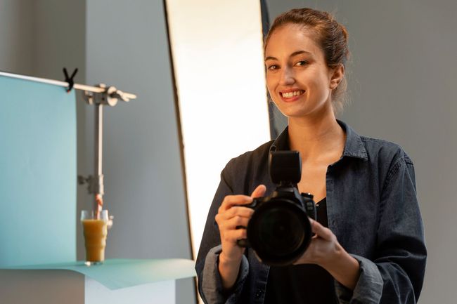 A woman is holding a camera in front of a glass of orange juice.