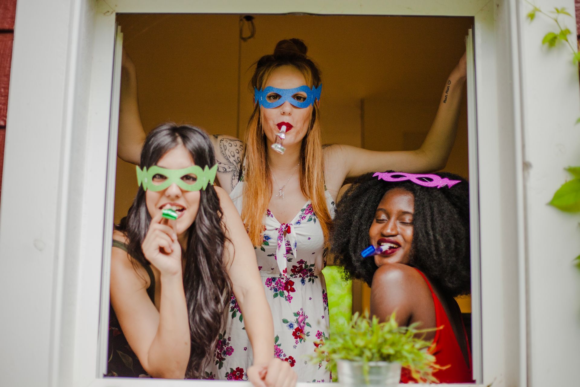 Three women wearing masks are blowing soap bubbles out of a window.