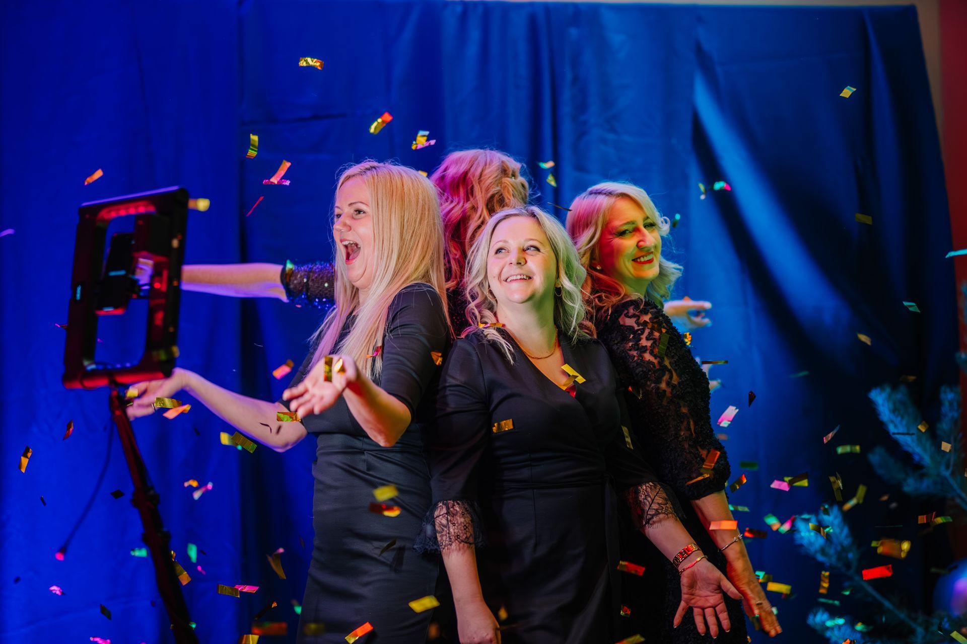 Three women are posing for a picture in a photo booth with confetti falling around them.