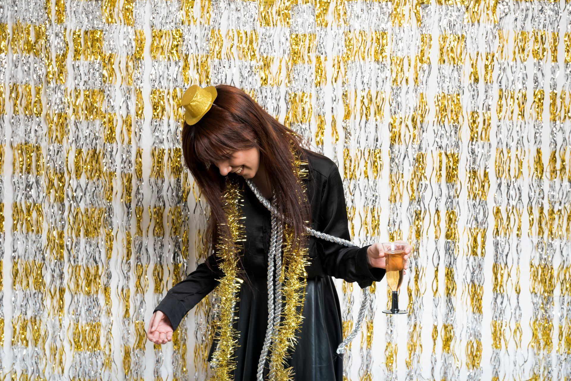 A woman is drinking champagne in front of a gold and silver curtain.