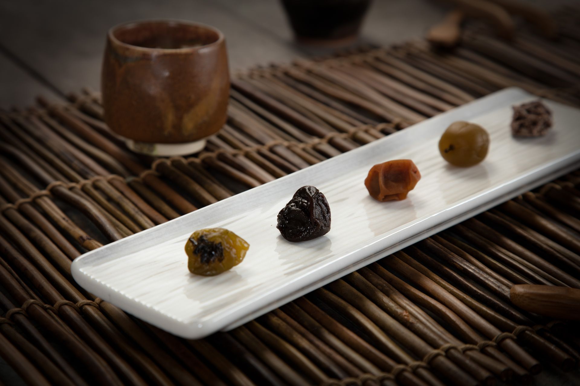 白色盤子上擺放著各種乾果，背景可以看到一個棕色杯子，盤子放在竹蓆上。