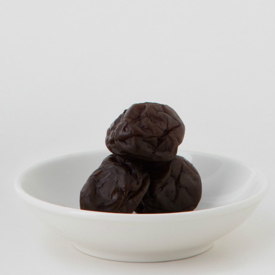 一袋乾梅子旁邊放著一小碟梅子；酒紅色包裝，白色背景。