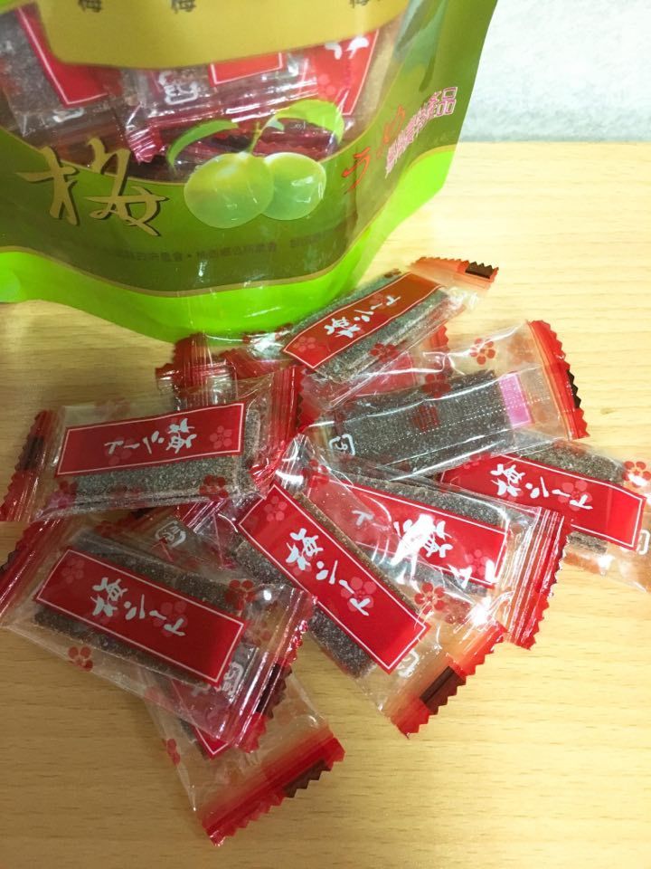 獨立包裝的梅子糖從一個半露在外的綠色袋子裡傾瀉而出，袋子放在木質表面上。
