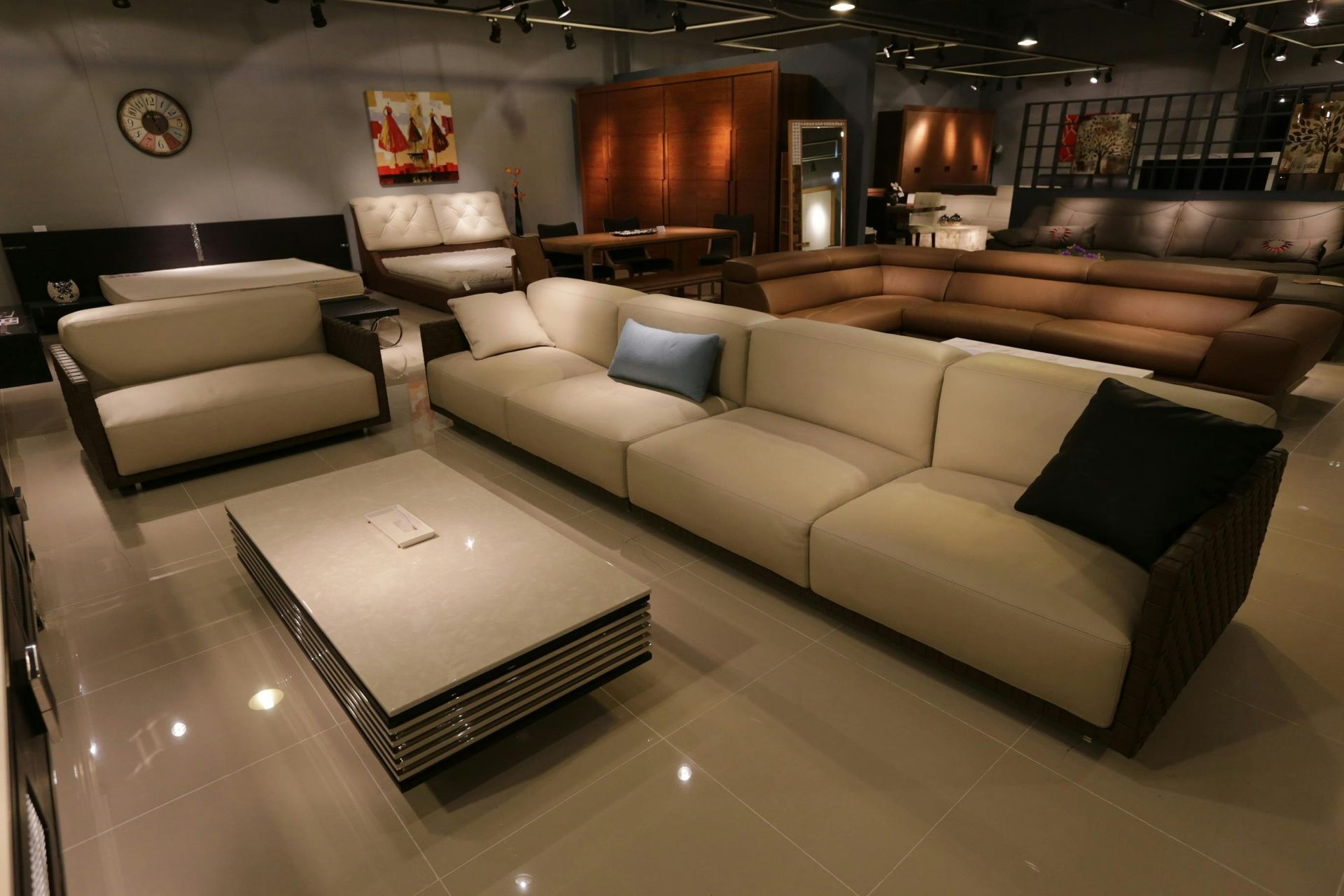 A showroom featuring a long cream sofa, a matching loveseat, and a central white coffee table on a tiled floor.