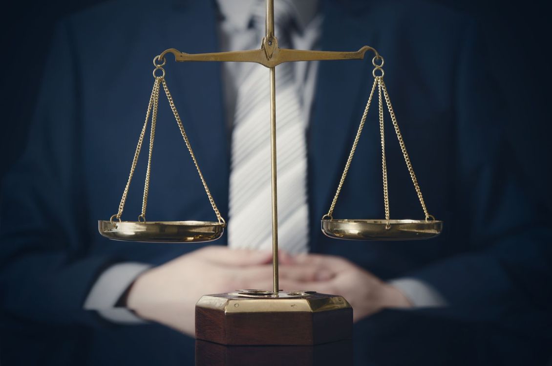 a man in a suit and tie sits in front of a scale of justice