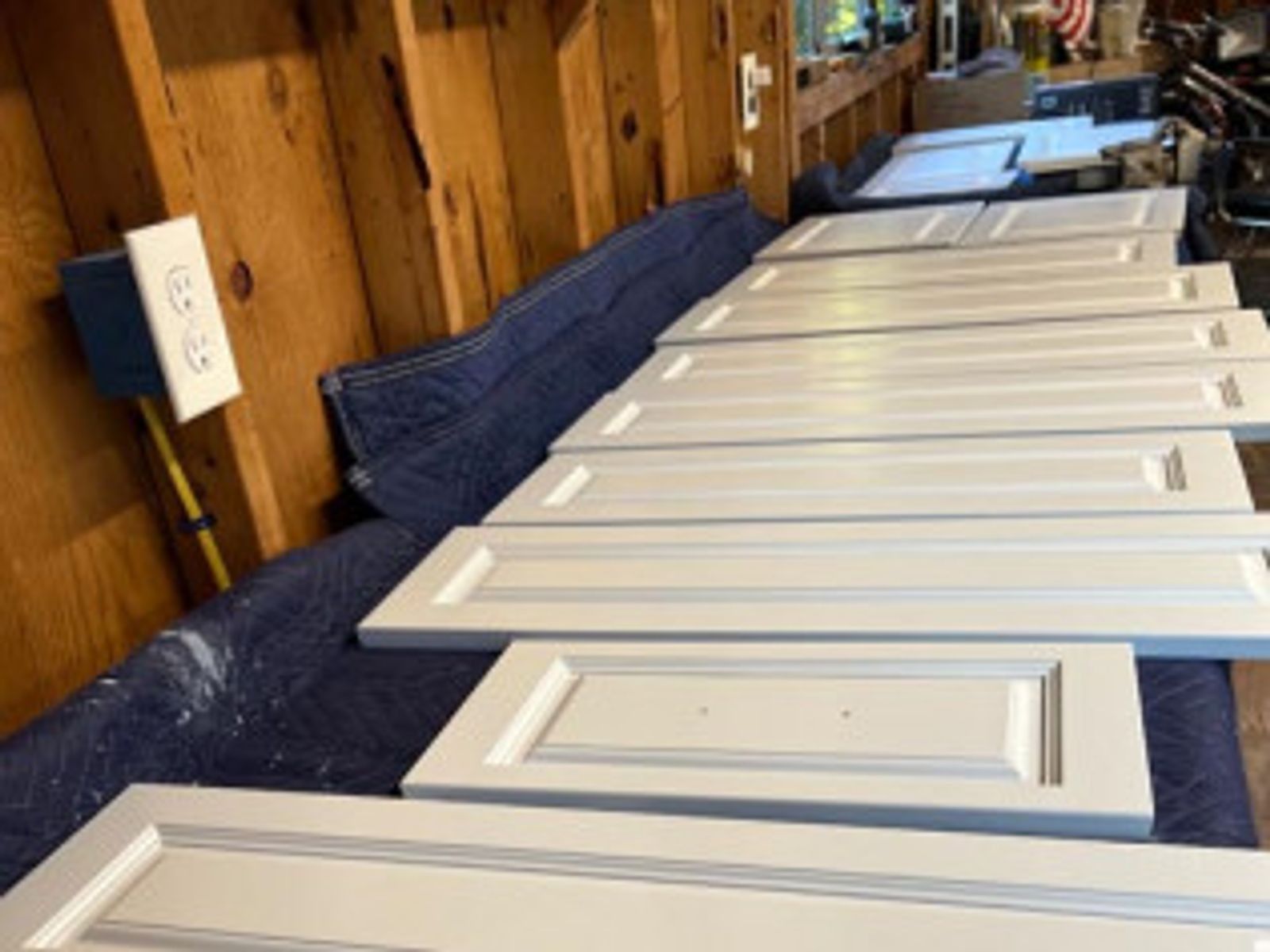 White cabinet doors laid out on a blue cloth in a garage, presumably for painting.