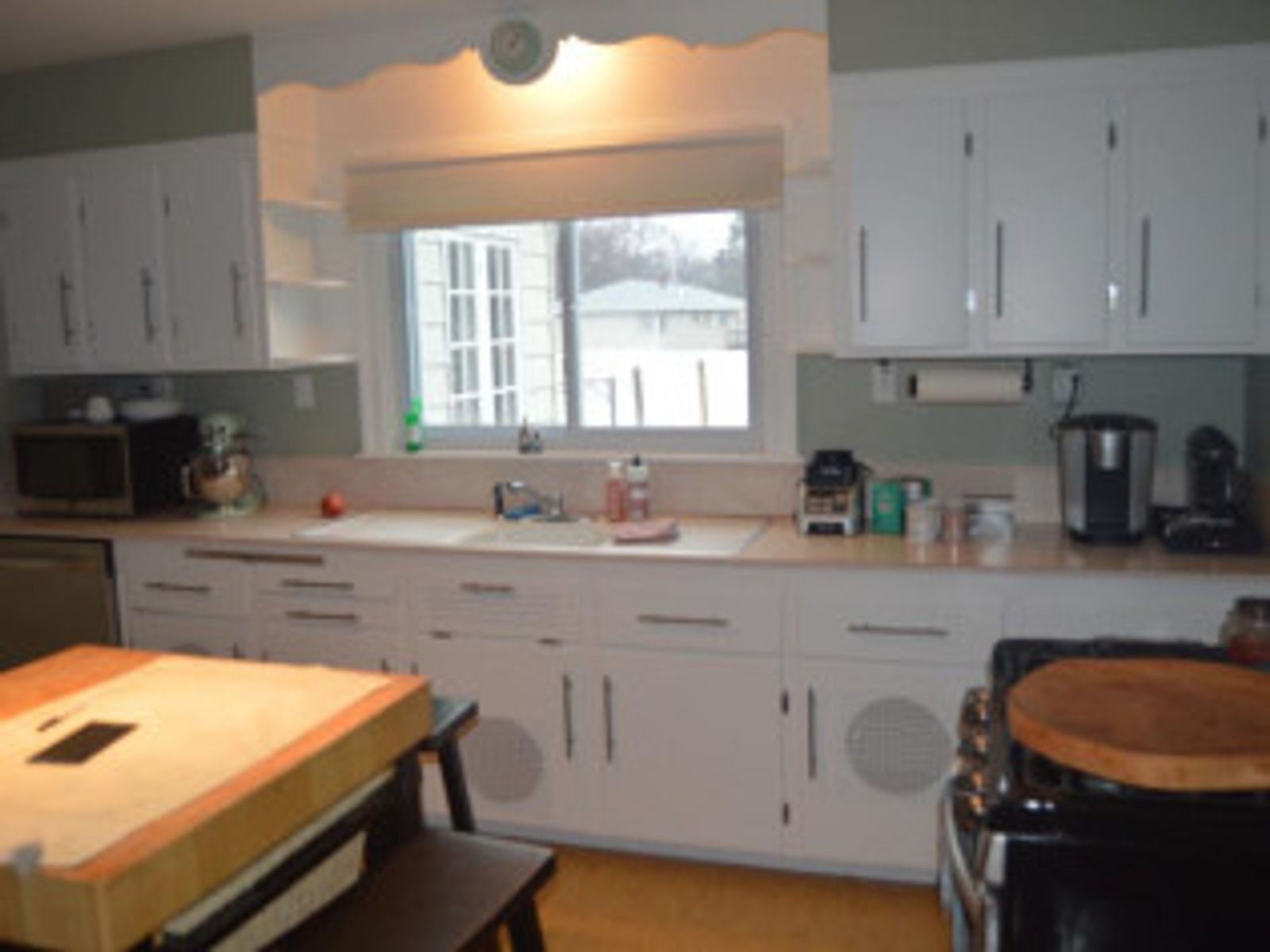 White kitchen with cabinets, a window, stove, and a wooden table.
