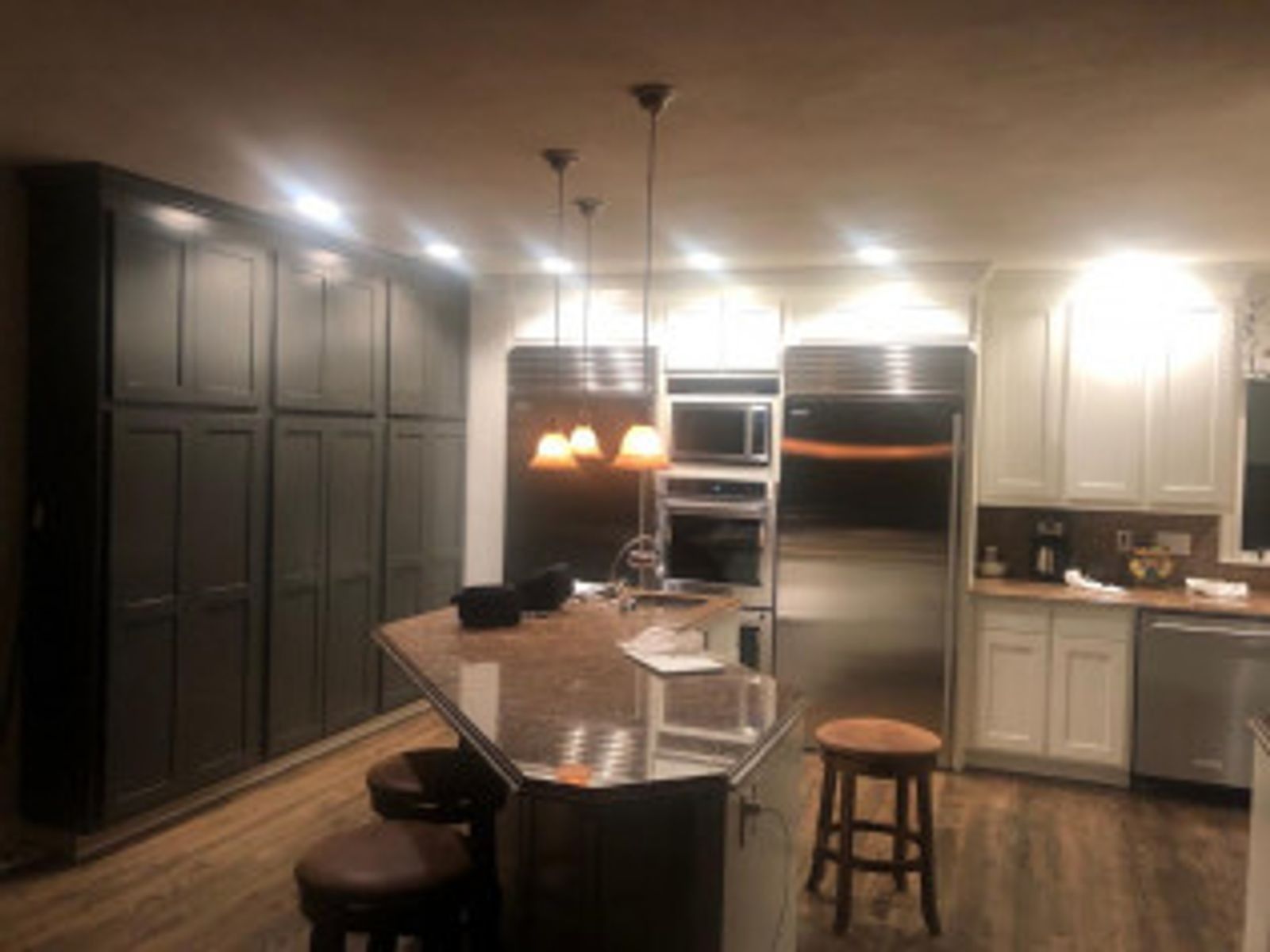 Kitchen with dark cabinets, stainless steel appliances, an island with stools, and pendant lights.