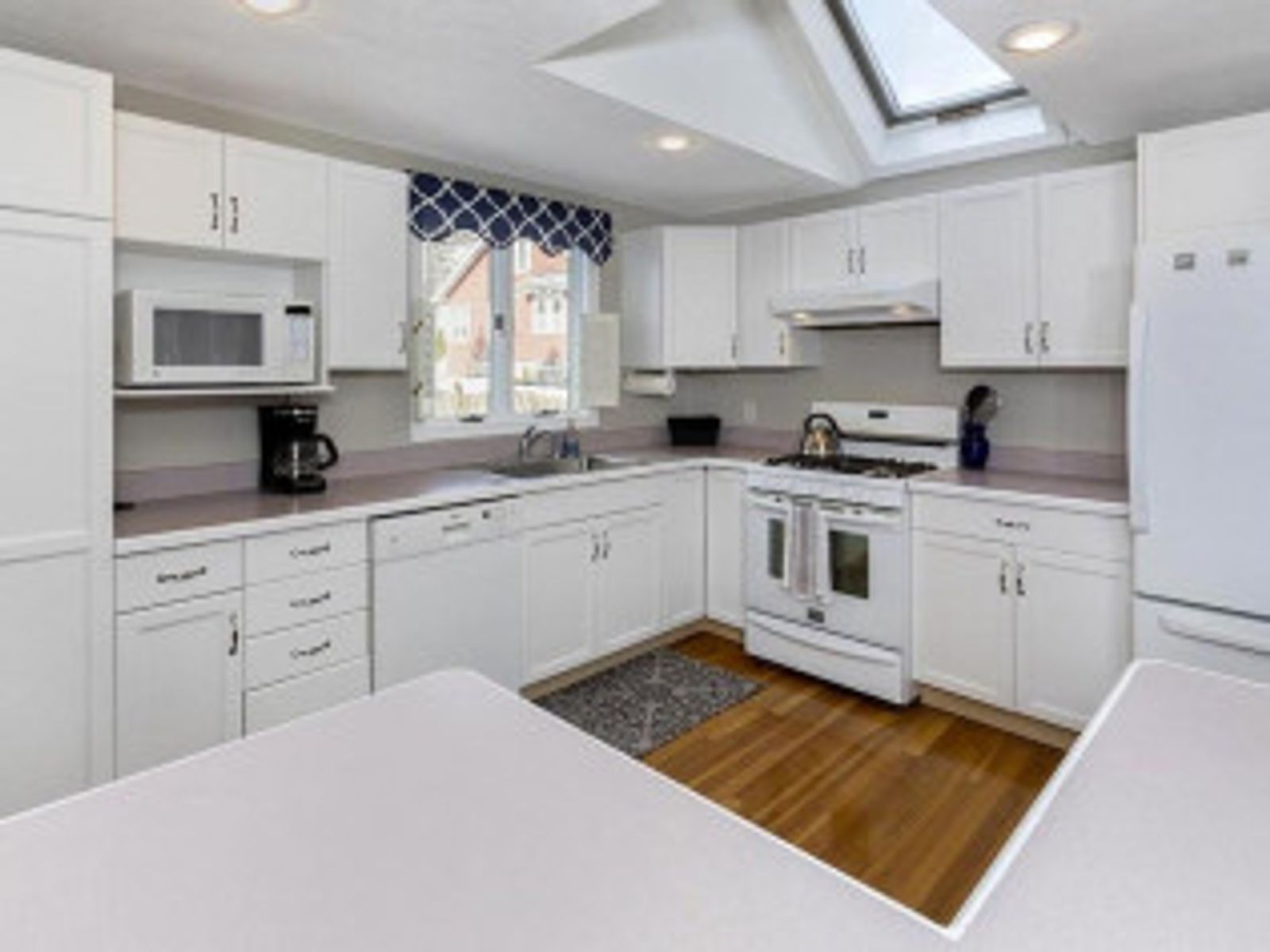 White kitchen with cabinets, appliances, wooden floor, and a skylight.